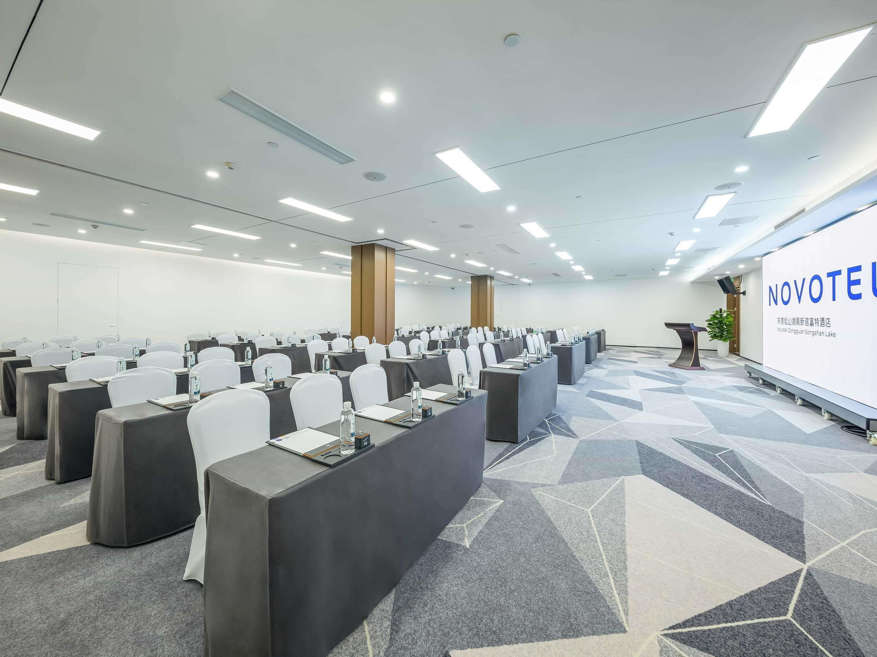 A conference room with rows of tables, chairs, and a presentation screen.