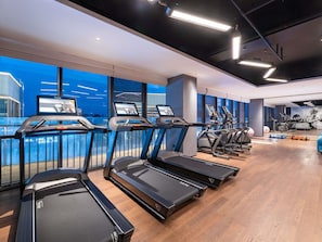 Un gimnasio con cintas de correr, bicicletas estáticas y un amplio ventanal con vistas a un cuerpo de agua.