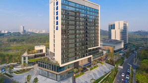 A modern hotel with a prominent vertical sign, extensive glass facade, and a landscaped surrounding. - Novotel Dongguan Songshan (Dongguan)