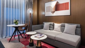 A modern hotel room with a sofa, two side tables, a floor lamp, and a large abstract painting on the wall. - Novotel Dongguan Songshan (Dongguan)