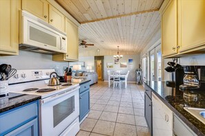 Een keuken met witte en blauwe kastjes, een fornuis, een magnetron en een eethoek met een tafel en stoelen.