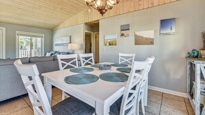 Een eetruimte met een witte tafel, witte stoelen en een kroonluchter. Er hangen foto’s aan de muur en staat een bijzettafeltje met decoratieve objecten.