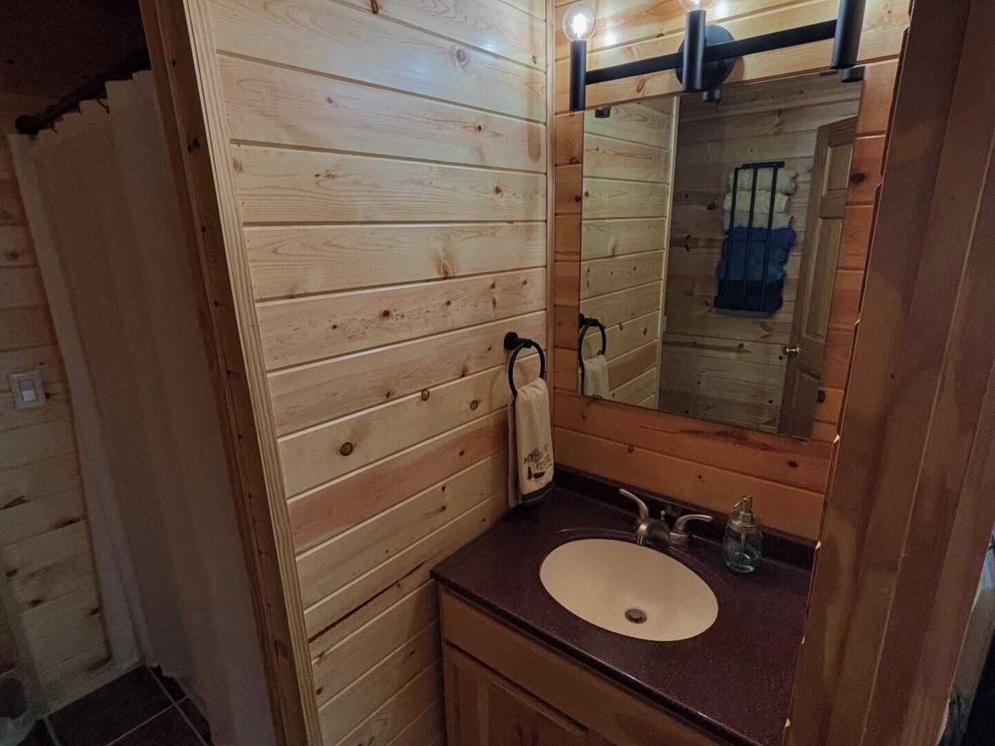 Ein Badezimmer einer Holzhütte mit einem Holztischchen, einem Waschbecken und einem Spiegel.