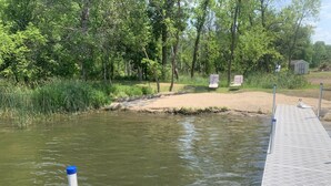 Een oever met een steiger die in het water reikt, omringd door bomen en een klein gebouw.