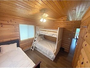 A wooden cabin room with bunk beds, a ladder, a window, and a ceiling fan.