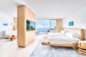 Una moderna camera d'hotel con un letto grande, una televisione, un angolo salotto con tavolo e sedie, e vista sul mare.