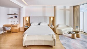 A modern hotel room with a large bed, a desk, a chair, a sofa, and a small table with a glass top. - The Maybourne Riviera (Roquebrune-Cap-Martin)