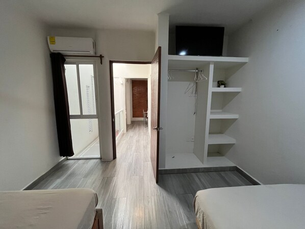 A hotel room with a bed, a wardrobe, a TV, and a hallway leading to another room.