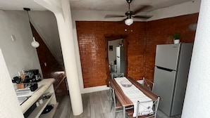 Una cucina compatta con un tavolo di legno, sedie, un frigorifero e una parete in mattoni.