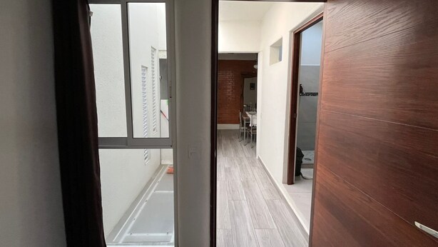 Un corridoio stretto con una porta scorrevole in vetro che dà su un balcone, una porta in legno sulla destra e un angolo cottura sullo sfondo.
