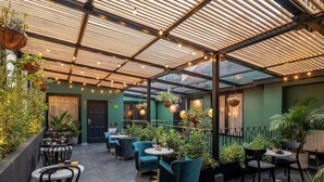 An outdoor patio with tables and chairs, potted plants, and hanging lights.