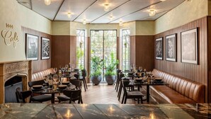 A restaurant with a fireplace, wooden paneling, and framed pictures on the walls. Tables are set with wine glasses and plates.