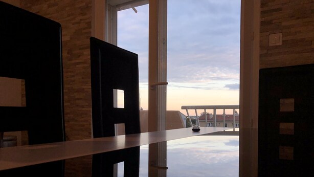 A room with a large window, a white railing, and a view of buildings and clouds. - Beautiful modern apartment near the sea (Frontignan)
