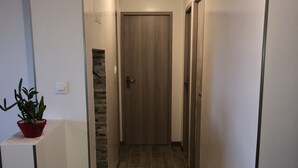 A narrow hallway with a wooden door at the end, a potted plant on the left, and a light fixture on the ceiling. - Beautiful modern apartment near the sea (Frontignan)