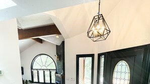 A spacious interior with a wooden floor, a black door with a stained glass window, and a hanging light fixture.