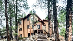 A wooden building with a staircase leading to a door, surrounded by trees and rocks.