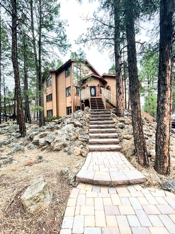 A wooden building with a staircase leading to a door, surrounded by trees and rocks.