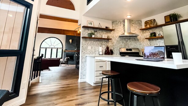 A modern kitchen with a central island, bar stools, and a chandelier.