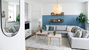 A modern living room with a grey sofa, two wooden tables, a white rug, and a blue accent wall. - Sfeervol Vakantiehuis in Centrum Yerseke (Yerseke)
