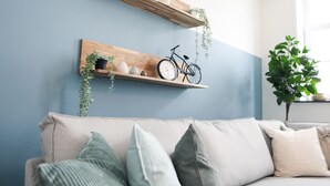 A living room with a light blue wall, a wooden shelf with decorative items, a bicycle, and a beige sofa with cushions. - Sfeervol Vakantiehuis in Centrum Yerseke (Yerseke)