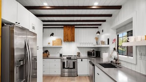 Een moderne keuken met roestvrijstalen apparatuur, witte kastjes en een houten balk.