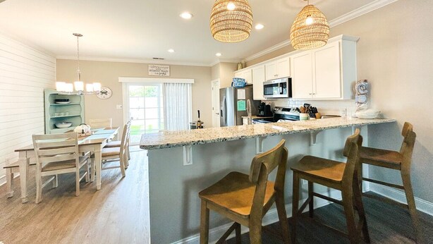 A kitchen with a central island, white cabinets, and pendant lighting. - Beach Getaway: Stunning, Family-Friendly w/ Pool. Walk to Shopping + Dining (Atlantic Beach)