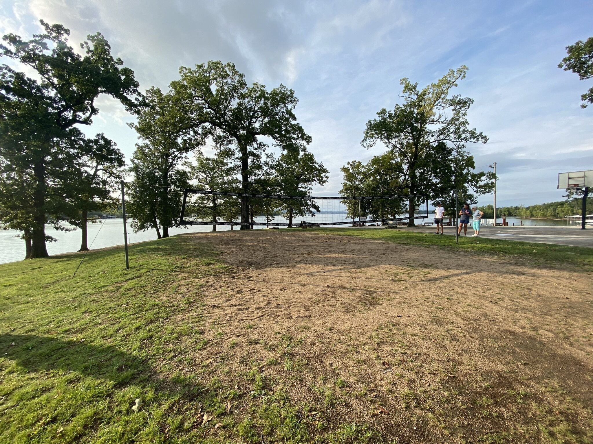 Un parque con una red de voleibol, árboles y un lago al fondo.