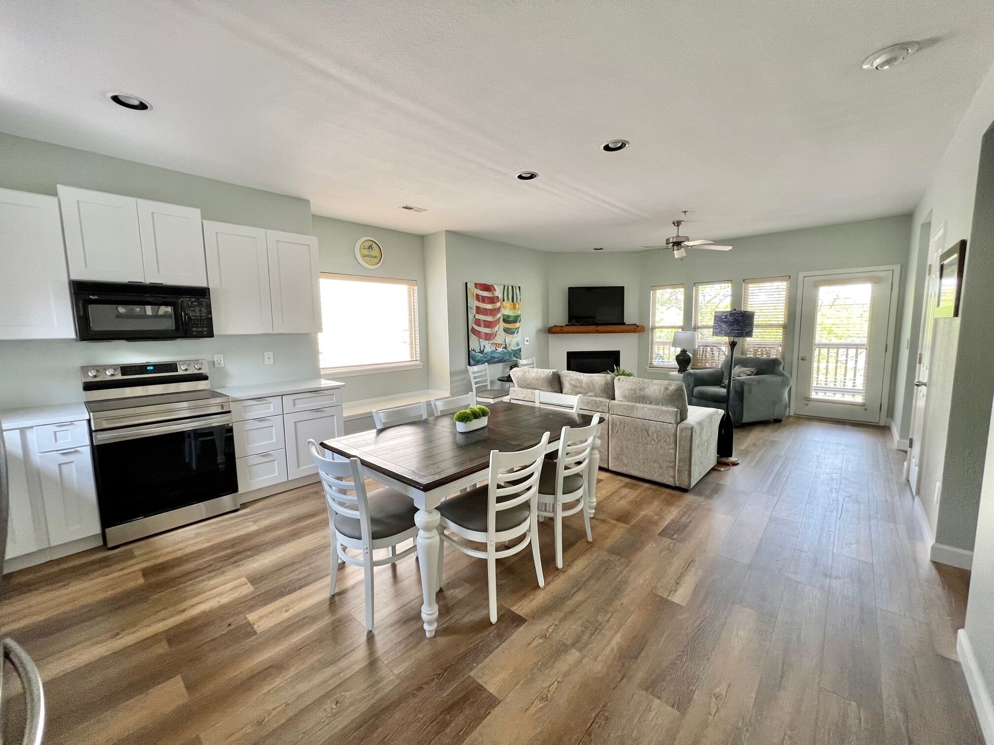 A spacious kitchen with white cabinets, a microwave, and a stove. There is a dining area with a wooden table and white chairs.
