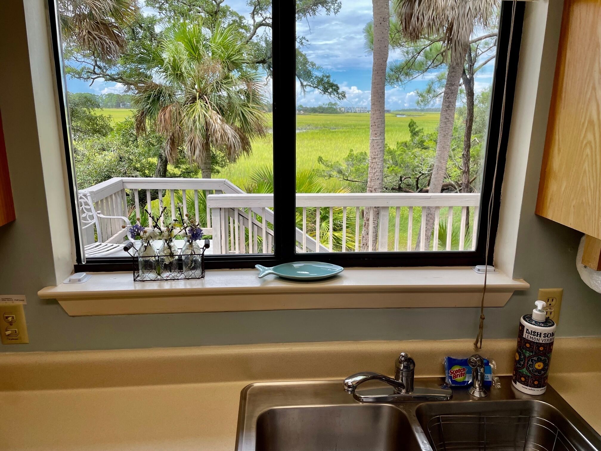 A kitchen with a window overlooking a deck and a view of a green landscape.