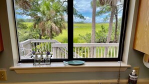 Une cuisine avec une fenêtre donnant sur une terrasse et offrant une vue sur un paysage verdoyant.