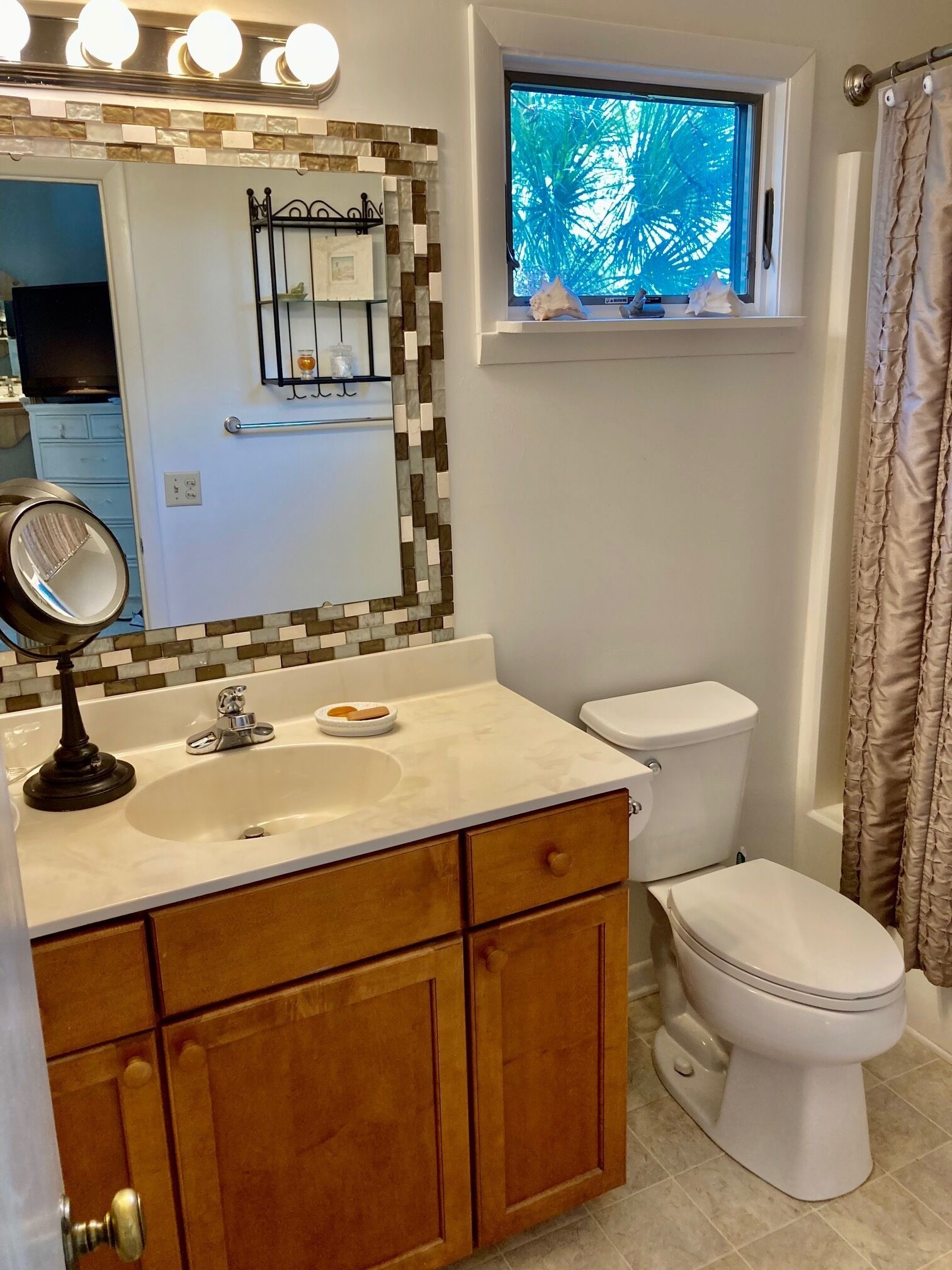 A bathroom with a white sink, mirror, and toilet. There is a window with a view of trees.