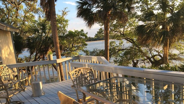 Une terrasse en bois avec une rambarde en verre donnant sur une étendue d’eau, entourée d’arbres.