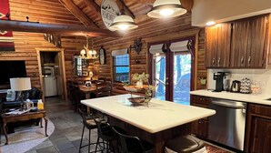 A rustic kitchen with wooden beams, a central island with bar stools, a refrigerator, and a coffee maker. - Luxury Log Cabin Living! AC, Kid & Pet Friendly, Fishing, Hiking, Golf (Pinetop)