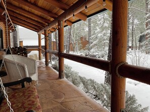 Un espace extérieur abrité, doté d’une balançoire, de poutres en bois et offrant une vue sur une forêt enneigée.
