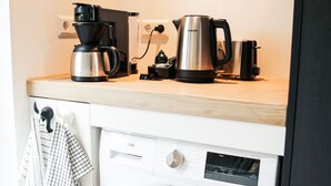 Cozinha compacta com cafeteira, chaleira e máquina de lavar.