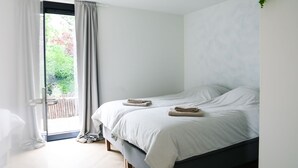 Quarto com uma cama, janela com cortinas e vista para o verde lá fora.