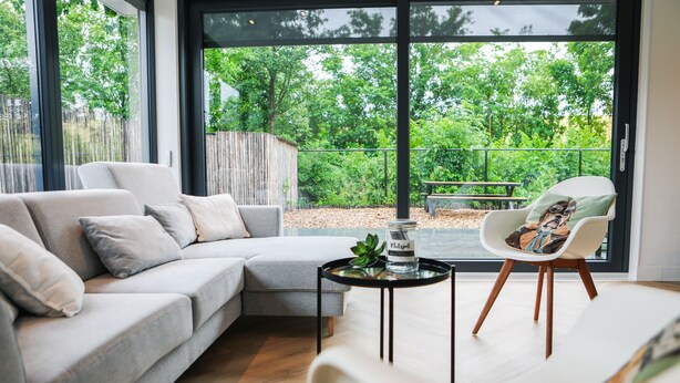 Uma sala de estar moderna com um sofá seccional cinza, uma poltrona branca e uma pequena mesa redonda com uma planta.