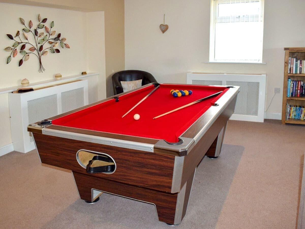 Une table de billard dans une pièce équipée d’un radiateur, d’une bibliothèque et d’un élément décoratif mural.