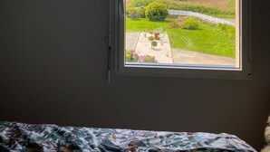 Een slaapkamer met een schuine plafond, een raam met uitzicht op een groen landschap en een lijst met een afbeelding aan de muur.