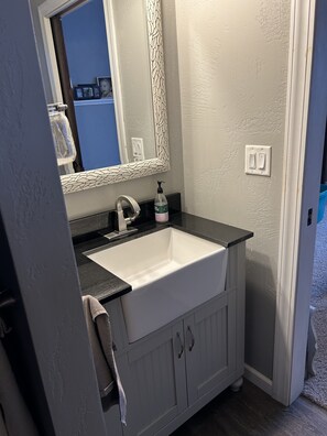 A bathroom with a white sink, dark countertop, and a mirror with a leaf pattern. There is a towel hanging on the door.