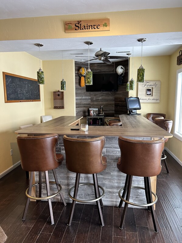 A dining area with a wooden table, three leather chairs, a ceiling fan, and a TV mounted on the wall.
