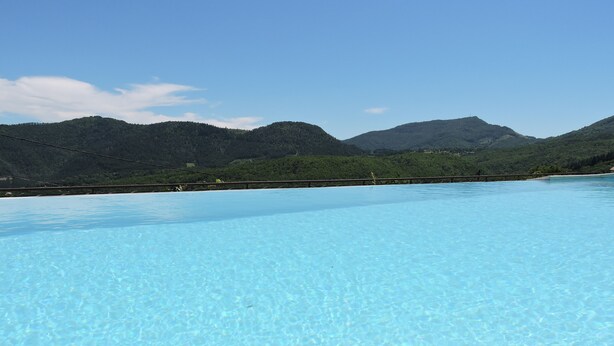 Una piscina azul cristalina con vistas a montañas verdes al fondo.