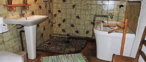 A bathroom with a white sink, a toilet, a shower with a wooden chair, and a patterned floor.