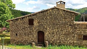 Un edificio de piedra con una puerta central y una ventana pequeña, rodeado de follaje.
