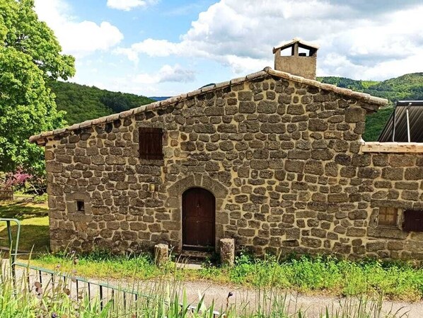 Un edificio de piedra con una puerta central y una ventana pequeña, rodeado de follaje.