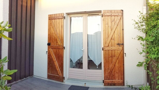 A wooden door with a glass panel, a metal doormat, and a small plant to the left. - Maisonnette Biscarrosse Plage 300m de Locéan (Biscarrosse)