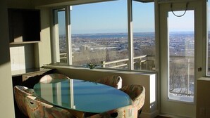 Un área de comedor con una mesa de vidrio y sillas estampadas, ventanas amplias con vista a la ciudad y una puerta con manija.