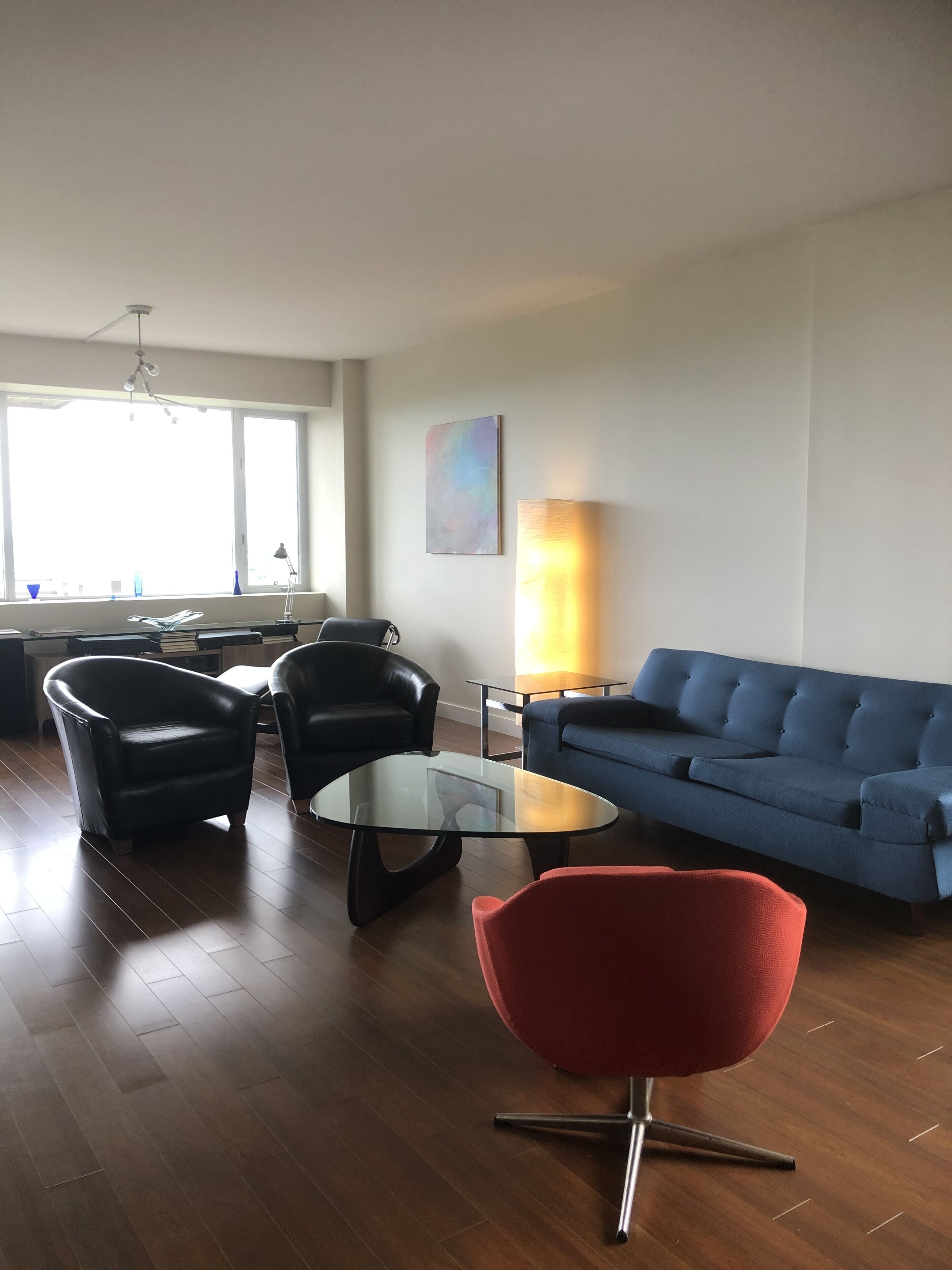 Una sala de estar con un sofá azul, una silla roja y dos sillas negras alrededor de una mesa de centro de vidrio.