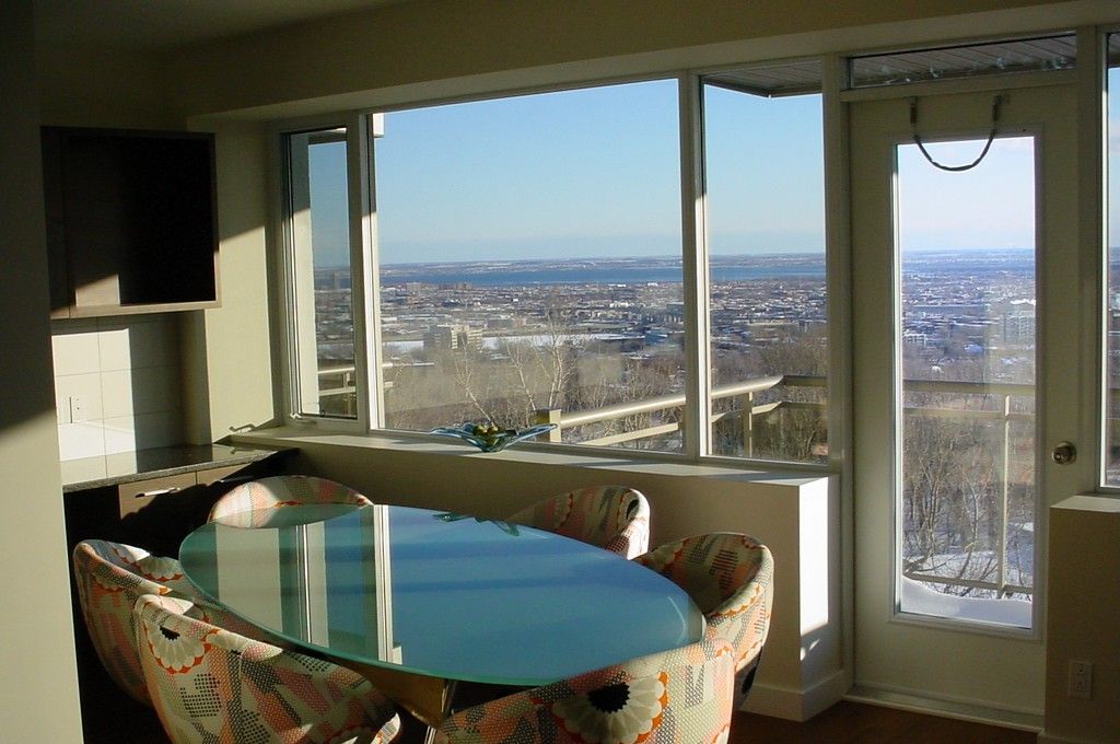 Un área de comedor con una mesa de vidrio y sillas estampadas, ventanas amplias con vista a la ciudad y una puerta con manija.