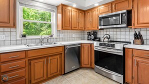 A modern kitchen with wooden cabinets, stainless steel appliances, and a window with a view of greenery. - Lakefront Home w/ Private Dock & MTB Trails Minutes from Bentonville (Bella Vista)